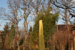 Holzskulptur, gelber Bambus, im Hintergrund die Saxdorfer Kirche